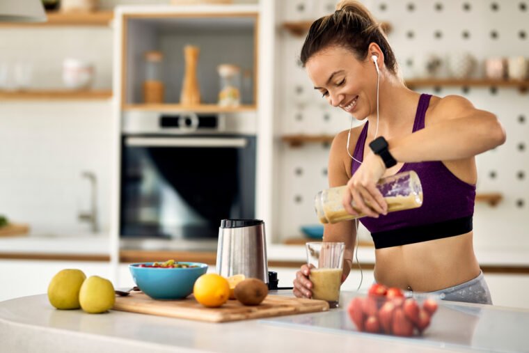 joven atletica feliz desayunando un batido de frutas en la cocina